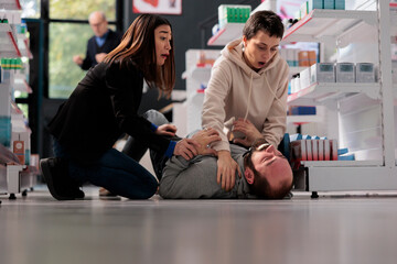 Frightened women rescuing man suffering from epilepsy attack, holding unconscious person and...