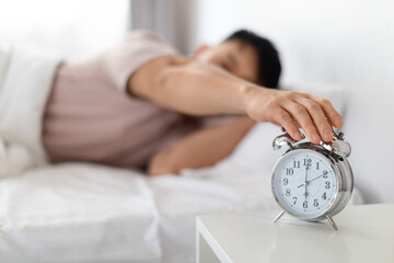 Asian man turning off alarm clock, waking up in morning