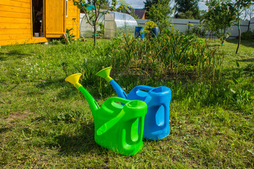 Two watering cans - green and blue on bright juicy grass on a sunny summer day . Concept gardening and plant care