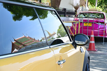 BANGKOK, THAILAND - July 20, 2023 : Thai Buddhist temple reflection in the mirror of a yellow car...