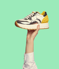 A woman's hand holding a fancy sneaker with a chunky insole, shiny silver inserts and a yellow...