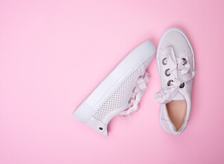Top view of Stylish white casual sneakers from perforated leather isolated on a soft pink...