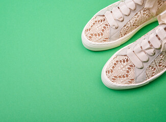 Delicate beige knitted design casual female sneakers on a green paper background with copy space. Creative minimalistic layout with footwear.
