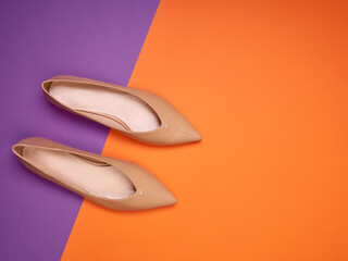 A pair of elegant light brown pointed-toe ballet flats on a two-colored background with copy space. Top view. Creative minimalistic layout with footwear.