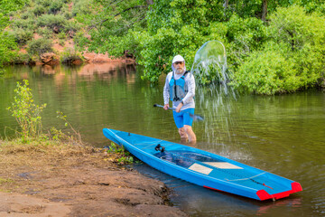male stand up paddler is splashing and rinsing his paddleboard, Horsetooth Reservoir near Fort...