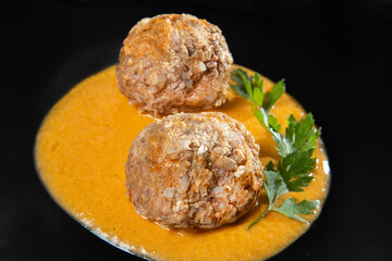 meatballs in sauce on a black plate.