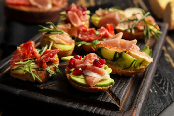 Board of tasty bruschettas with ham on dark wooden background, closeup
