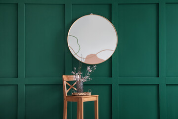 Vase with blooming branches on stool near mirror in room