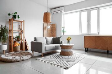 Interior of light living room with grey sofa, shelving unit and window