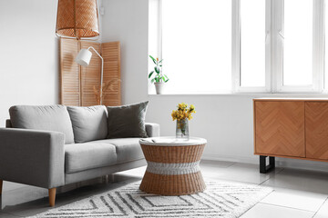 Interior of light living room with grey sofa, table and window