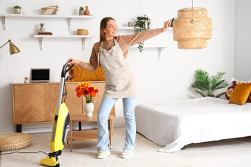 Young woman with vacuum cleaner dancing in bedroom