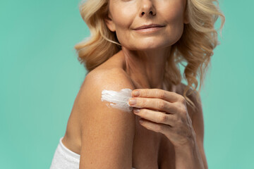 Close-up of mature woman applying anti-aging smoothing moisturizer cream on her body