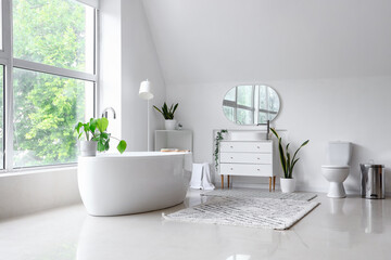 Fototapeta na wymiar Interior of light bathroom with bathtub, sink on chest of drawers and toilet bowl