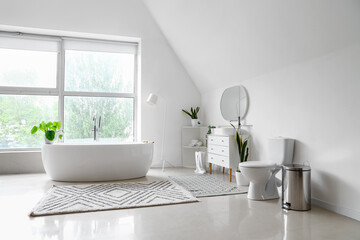 Interior of light bathroom with bathtub, sink on chest of drawers and toilet bowl