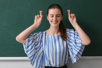 Female teacher crossing fingers near chalkboard in classroom