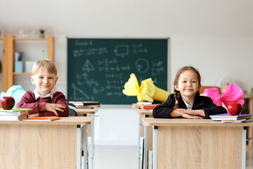 Happy classmates with school cones sitting at desks in classroom