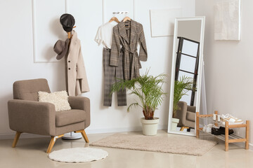 Interior of light hallway with mirror, rack and grey armchair