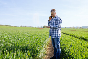 A male farmer stands in a field and talks on the phone. Modern technologies in agriculture