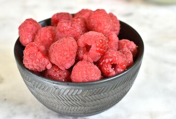 black bowl with raspberries on marble white table