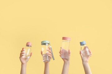 Women holding sports bottles with clean water on yellow background