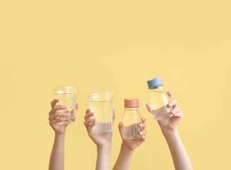 Women holding sports bottles and glasses with clean water on yellow background