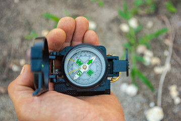 Kompas - busola z przyrządami celowniczymi i zielonymi fosforyzującymi napisami i oznaczeniem leżąca na dłoni podróżnika . Marsz na azymut - orientacja w terenie.  