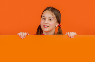 smiling child behind blank orange paper with copy space for advertisement