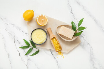Board with bowl of lemon body scrub, soap and sea salt on grunge white background