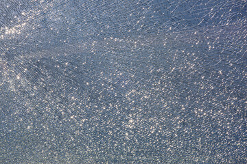 broken tempered glass in cracks, spoiled glass surface texture on blue sky background, shine from bright light, close-up.