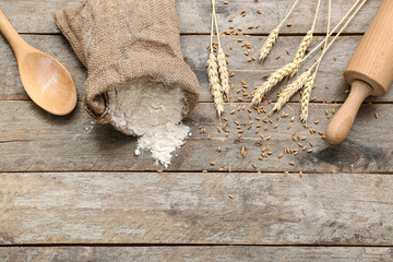 Wheat flour in sack, rolling pin and spoon on wooden background