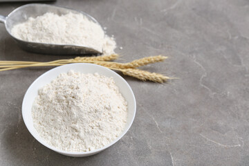 Bowl with wheat flour and spikelets on grey table, closeup