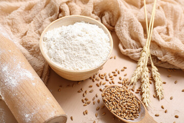 Flour, wheat and rolling pin on beige background