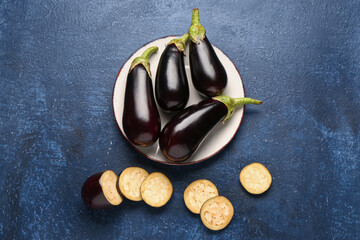 Plate with fresh eggplants on blue background
