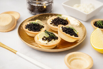 Plate of tasty tartlets with black caviar on grey background