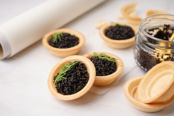 Tasty tartlets with black caviar on grey background