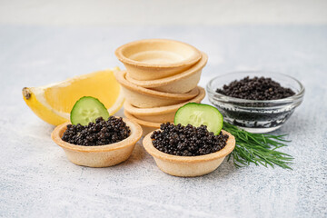 Tasty tartlets with black caviar on grey background