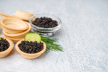 Tasty tartlets with black caviar on grey background