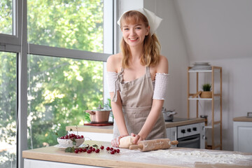 Bowl with cherries and happy beautiful woman kneading dough in kitchen