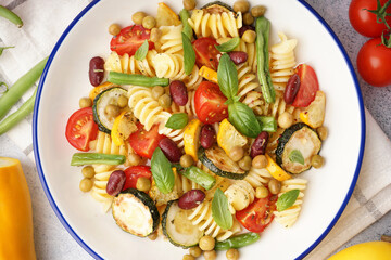 Bowl of tasty pasta salad with tomatoes and basil on white background