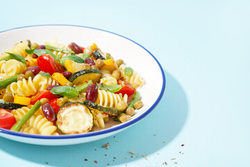 Bowl of tasty pasta salad with tomatoes and basil on blue background