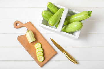 Board and basket with fresh green zucchini on white wooden background