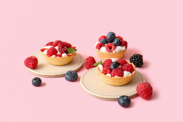 Tasty tartlets with whipped cream and berries on pink background