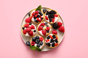 Plate of tasty tartlets with whipped cream and berries on pink background