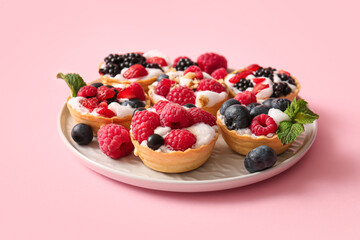 Plate of tasty tartlets with whipped cream and berries on pink background