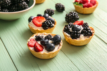 Tasty tartlets with whipped cream and berries on green wooden background
