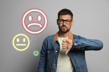 Complaint. Dissatisfied man showing thumbs-down on grey background. Illustrations of sad, neutral and happy faces near him