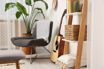 Spring atmosphere. Wooden shelving unit, acoustic guitar and comfortable chair in stylish room