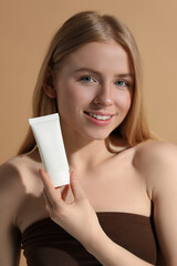 Beautiful young woman holding sun protection cream on beige background