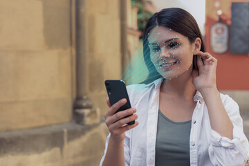 Woman using smartphone with facial recognition system on street. Security application scanning her face for approving owner's identity