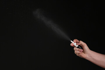 Nasal congestion. Woman spraying remedy from bottle on black background, closeup with space for text